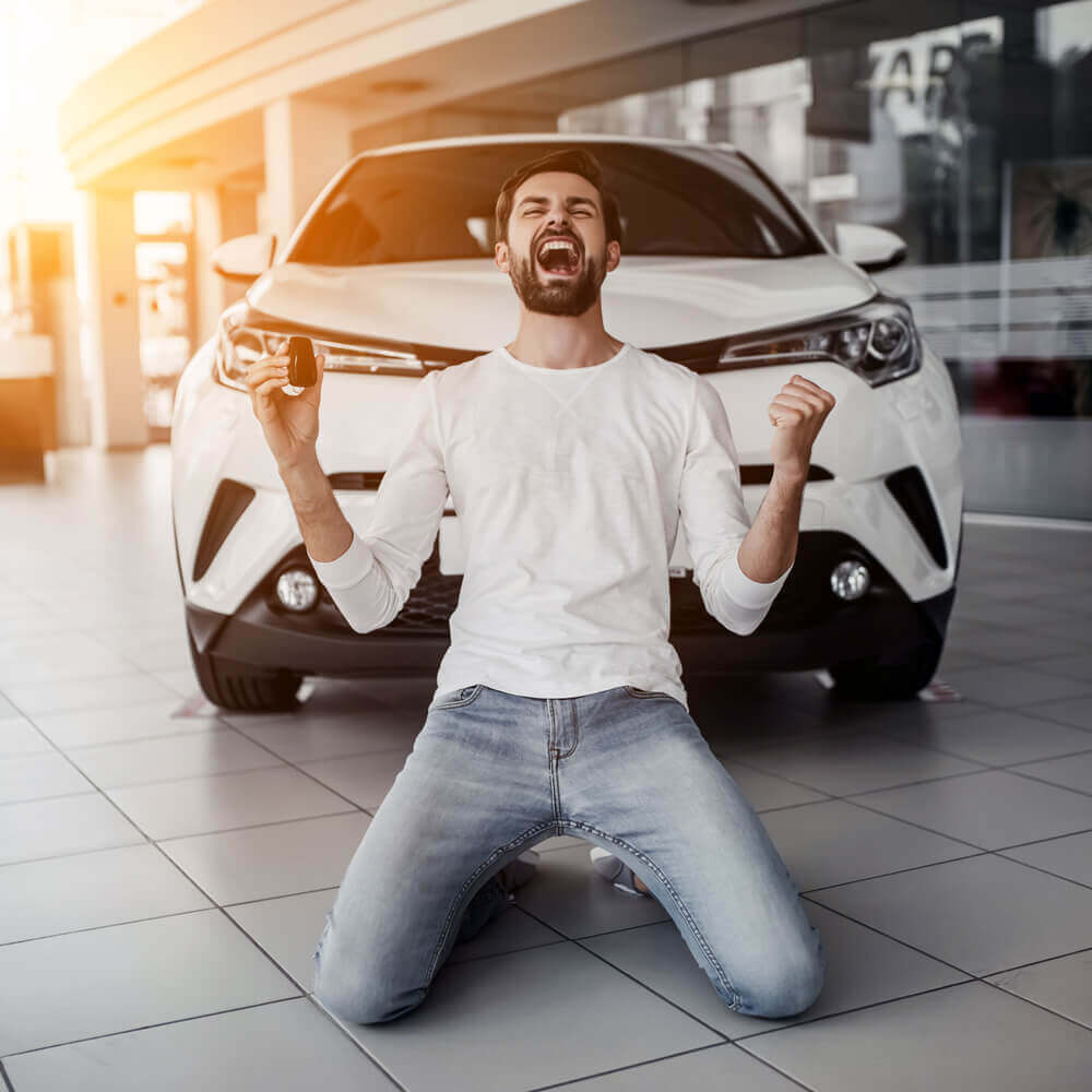 Man on his knees shouting for joy after buying a car